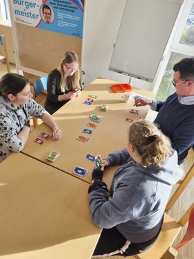 Bürgermeister Peter Jung sitzt mit drei Mädchen am Tisch. Sie spielen das Kartenspiel Skip-Bo. 